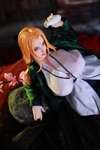 Tsunade-Mini-Sex-Puppe posiert bekleidet in einem inszenierten Raum, blondes Haar und blauer Stirndiamant