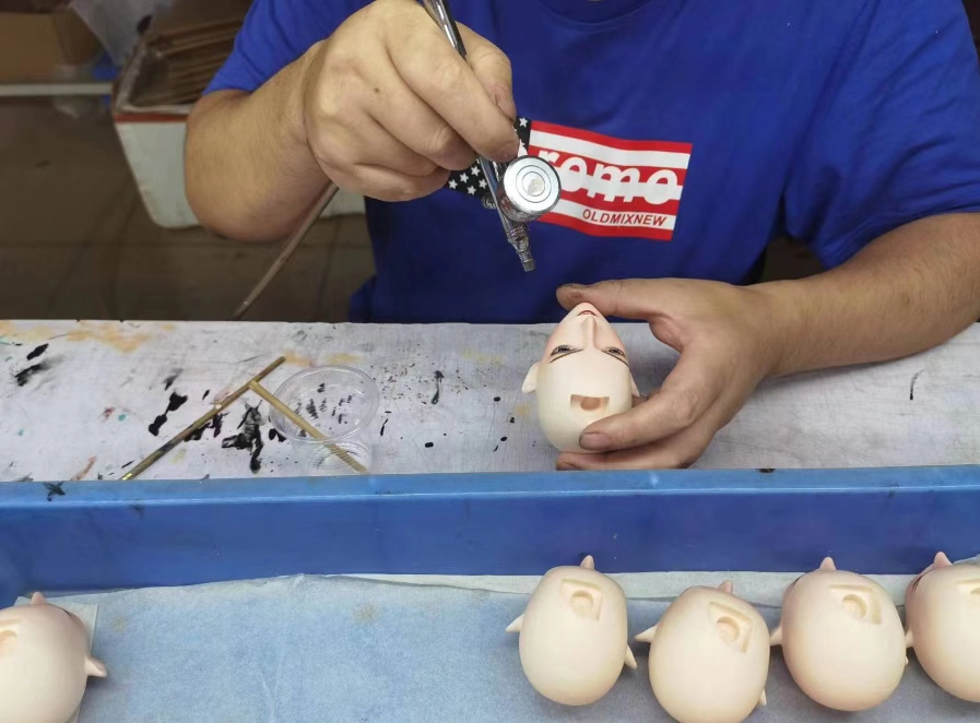 Artist airbrushing a row of unpainted PU figure doll heads