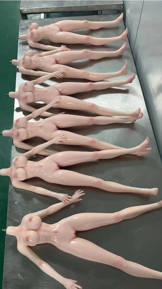 Row of freshly demolded raw silicone mini doll bodies on a steel workshop table